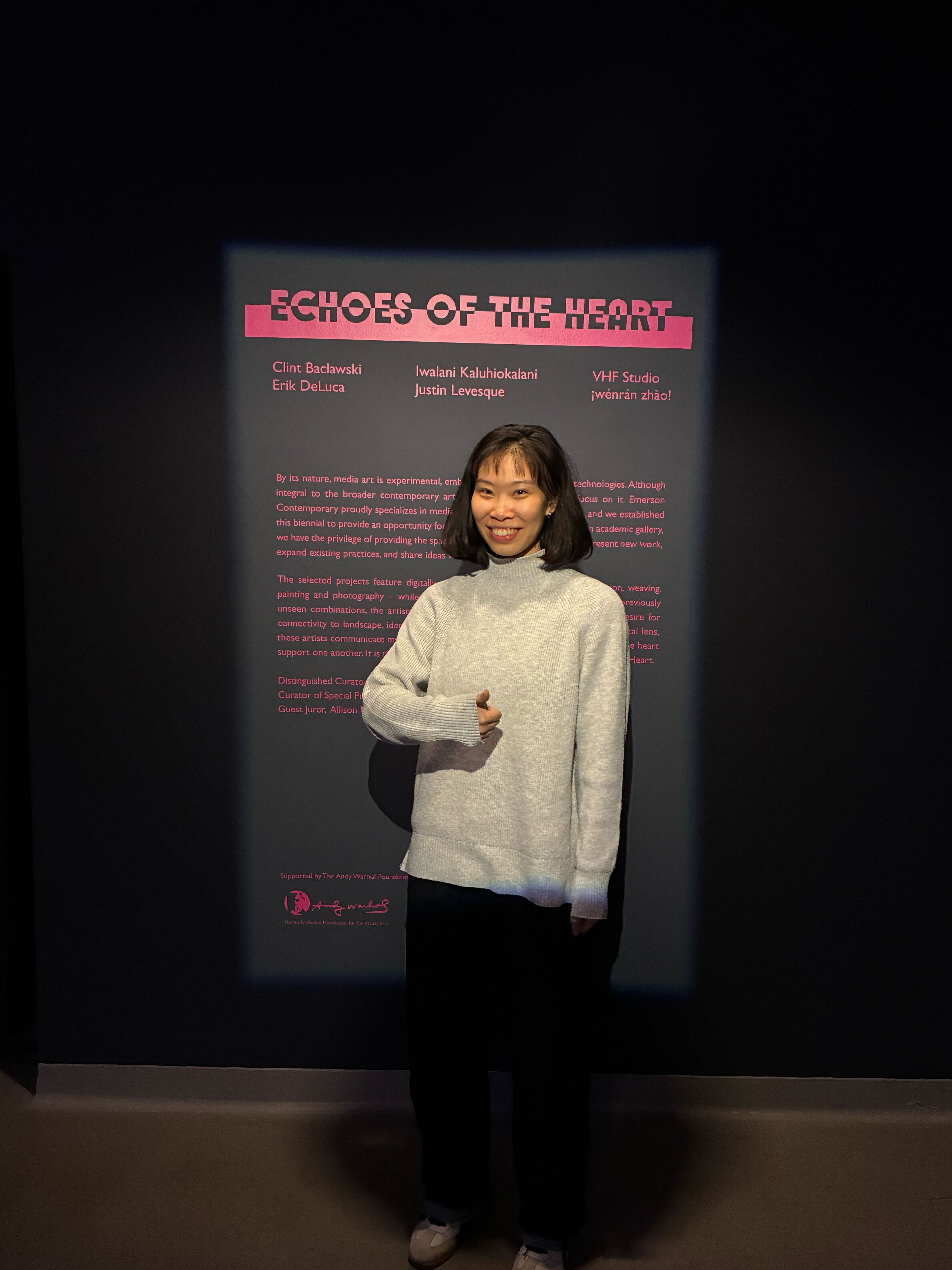 Karlie smiling and doing a thumbs up in front of her exhibit text panel